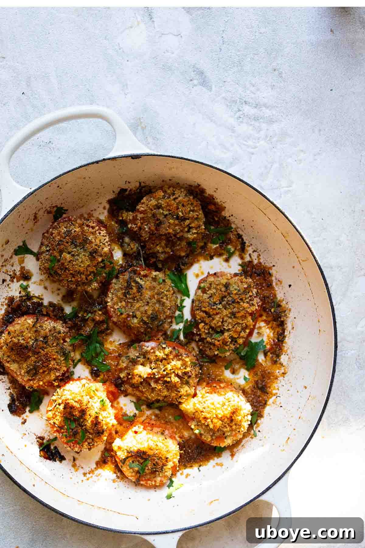 Sun-Kissed Roasted Tomatoes with Garlic-Herb Crumble 2 breadcrumb stuffed tomatoes in a white cast iron pot.