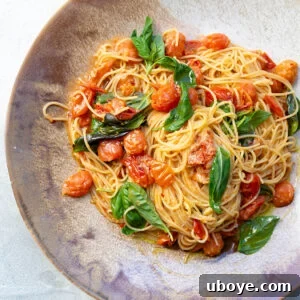 Close-up of the finished cherry tomato and basil pasta, glistening with sauce and topped with fresh basil.