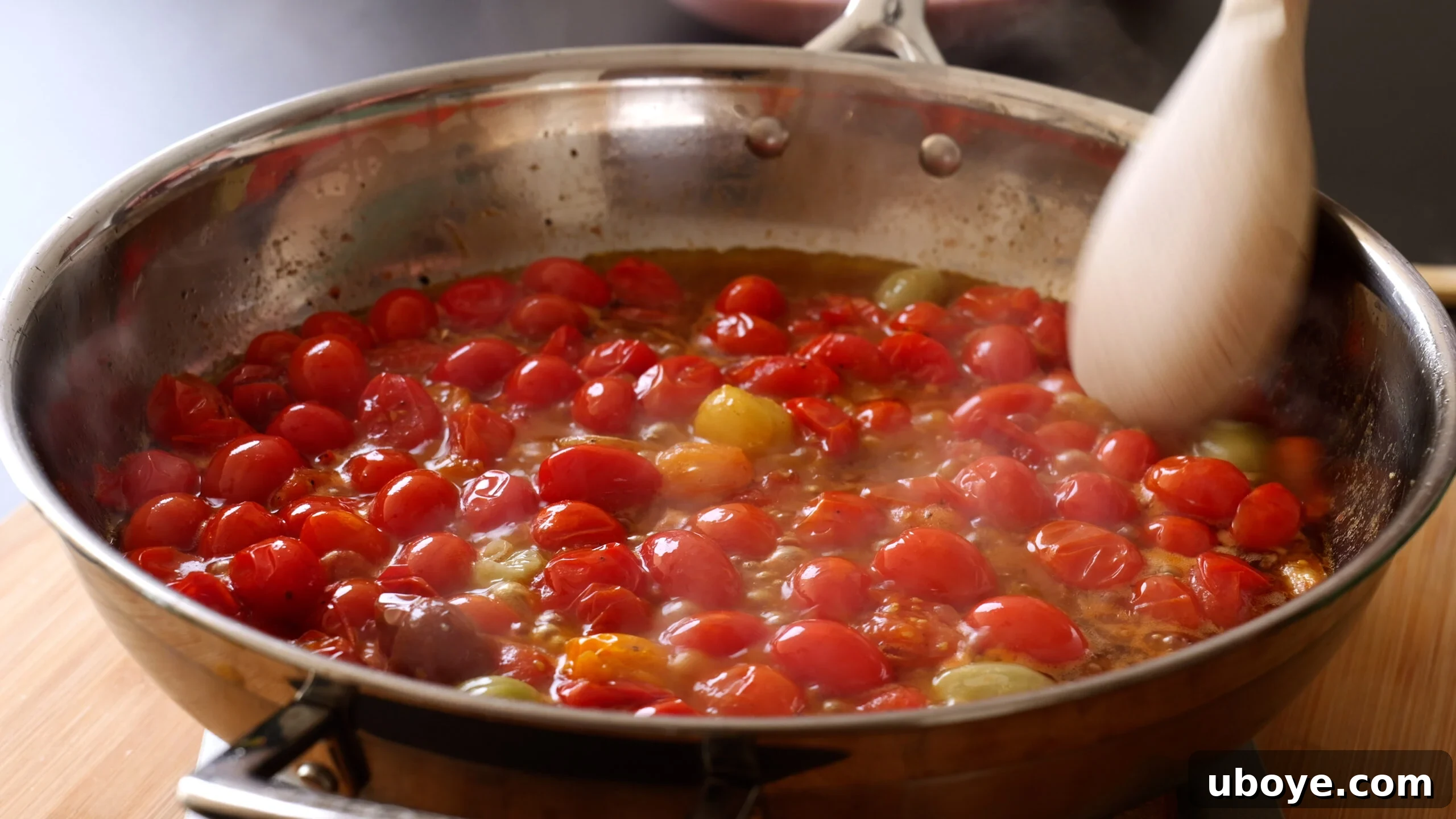 Garden Fresh Cherry Tomato Basil Pasta 5 Vibrant cherry tomatoes are sizzling in a large stainless steel pan, some beginning to blister and burst, releasing their sweet juices to form a rich, jammy sauce.