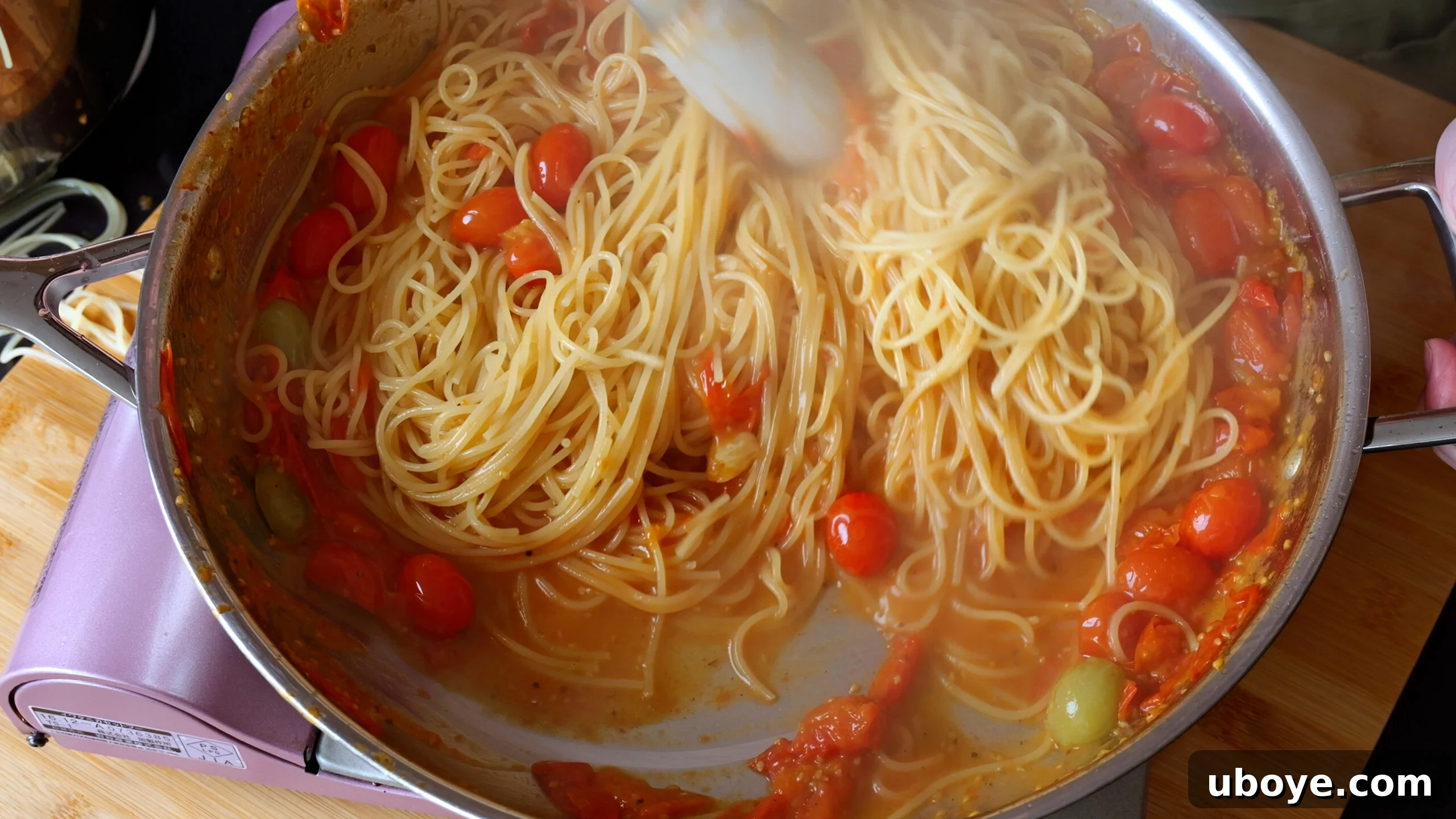 Garden Fresh Cherry Tomato Basil Pasta 6 Al dente spaghetti is being tossed into the vibrant cherry tomato and basil sauce in a large stainless steel pan, absorbing the rich flavors.