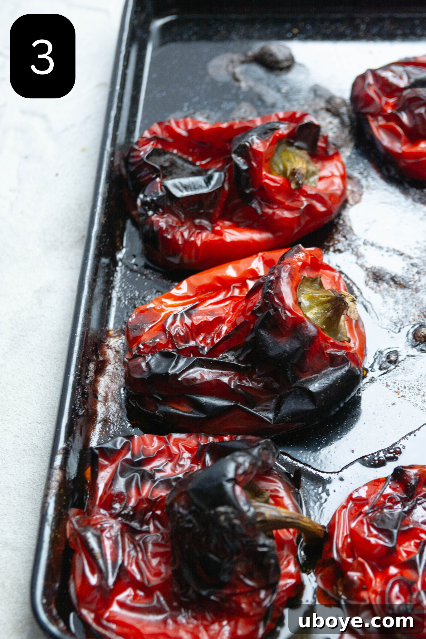 Fiery Feta and Red Pepper Dip 6 Charred red bell peppers cooling on a baking tray after roasting, showing their blackened skins.