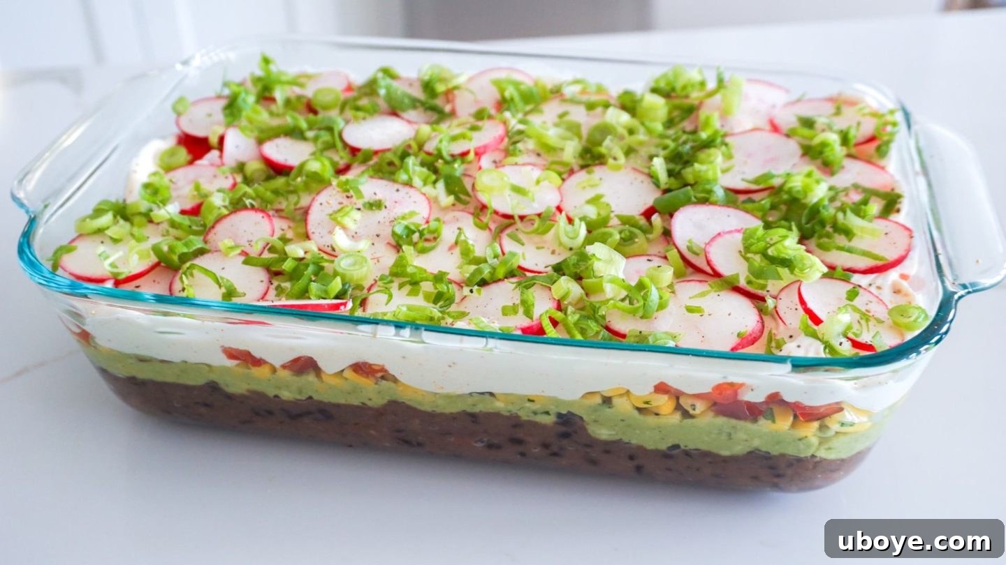 Epic Vegan 7 Layer Dip 2 Vibrant Vegan 7 Layer Dip in a clear glass casserole dish, ready to be served with tortilla chips on a white countertop.