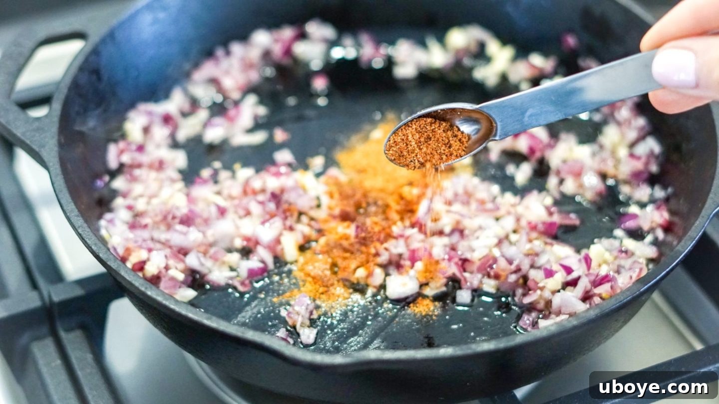 Epic Vegan 7 Layer Dip 3 Sautéed red onions and minced garlic cooking in a pan with taco seasoning, forming the flavorful base for refried beans.