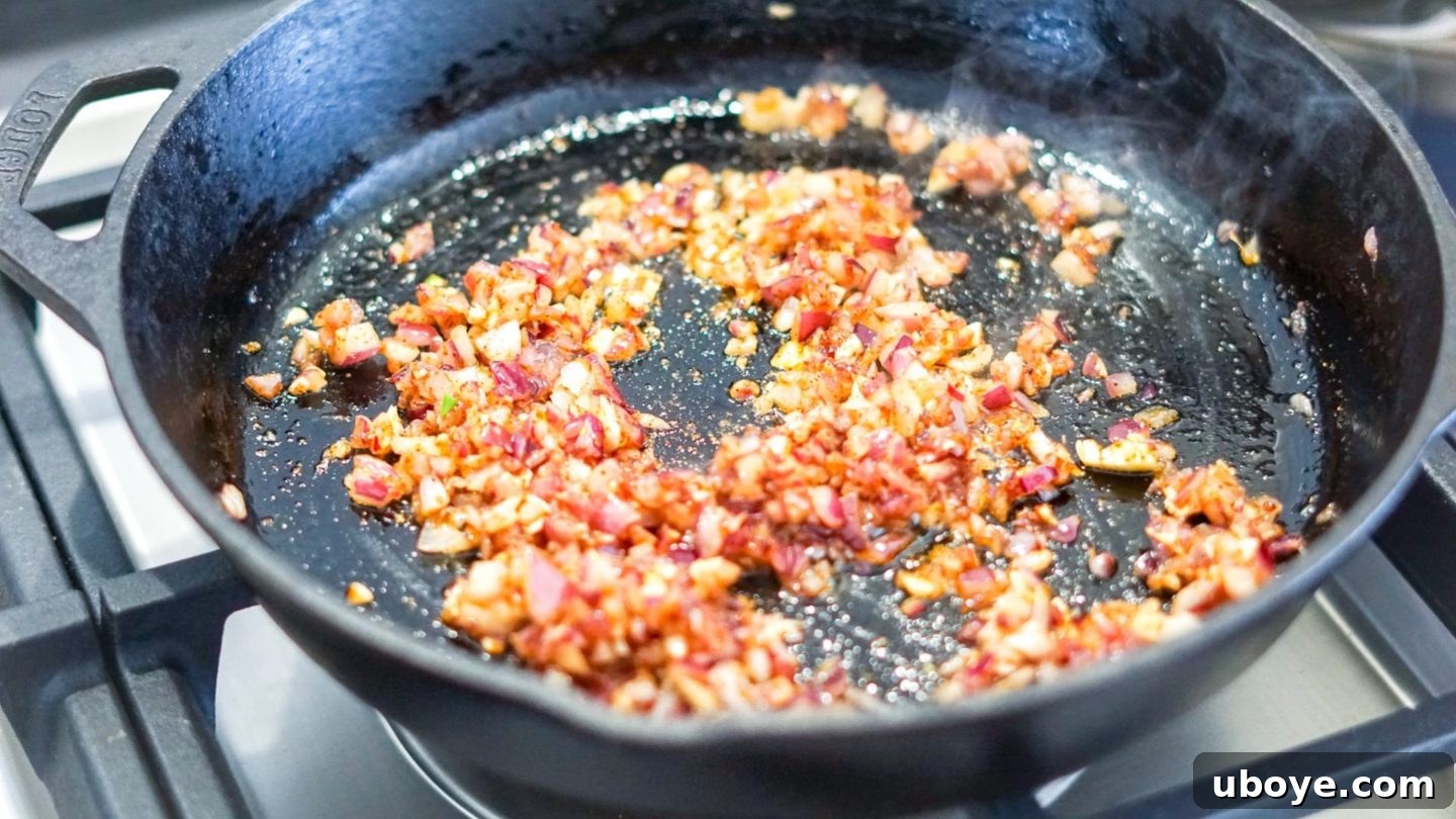 Epic Vegan 7 Layer Dip 4 Taco seasoning being added to sautéed onions and garlic in a pan, before the beans are introduced for maximum flavor.