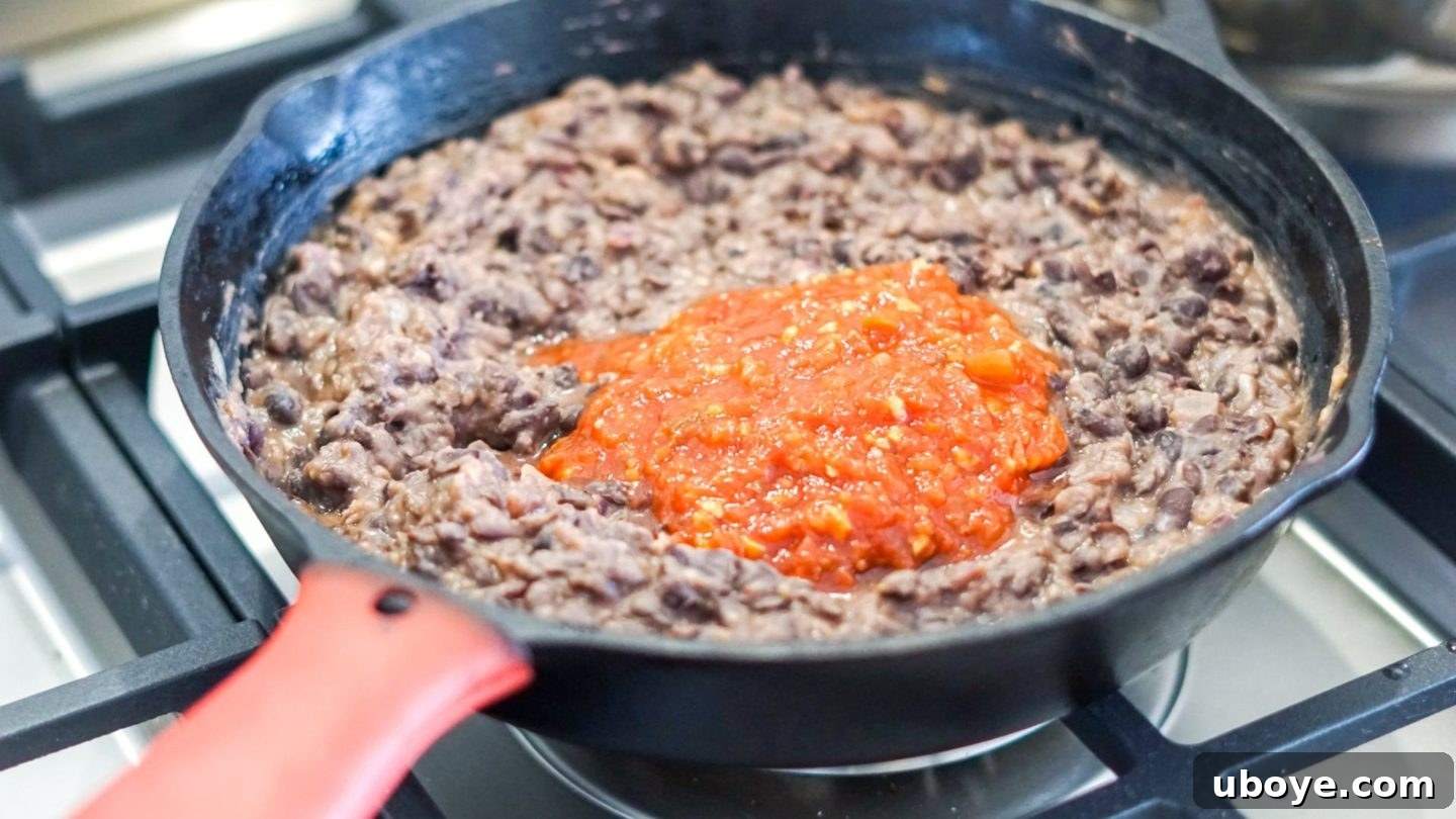 Epic Vegan 7 Layer Dip 5 Black beans, water, salt, and salsa being added to the pan with cooked spices, ready to be mashed into refried beans.