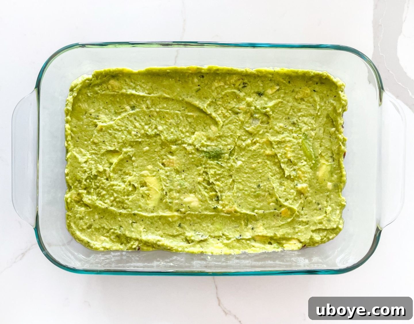 Epic Vegan 7 Layer Dip 7 Freshly made guacamole spread as the second layer in a glass casserole dish, atop the refried beans.