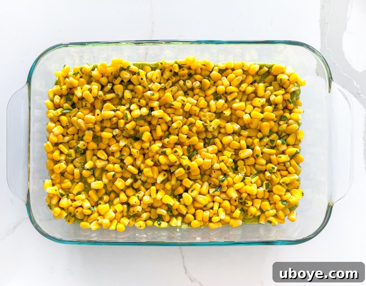 Epic Vegan 7 Layer Dip 9 Seasoned yellow corn spread evenly over the guacamole layer in a glass dish.