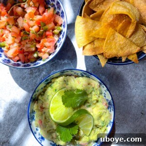 Three bowls of guacamole, salsa, and chips on a blue counter
