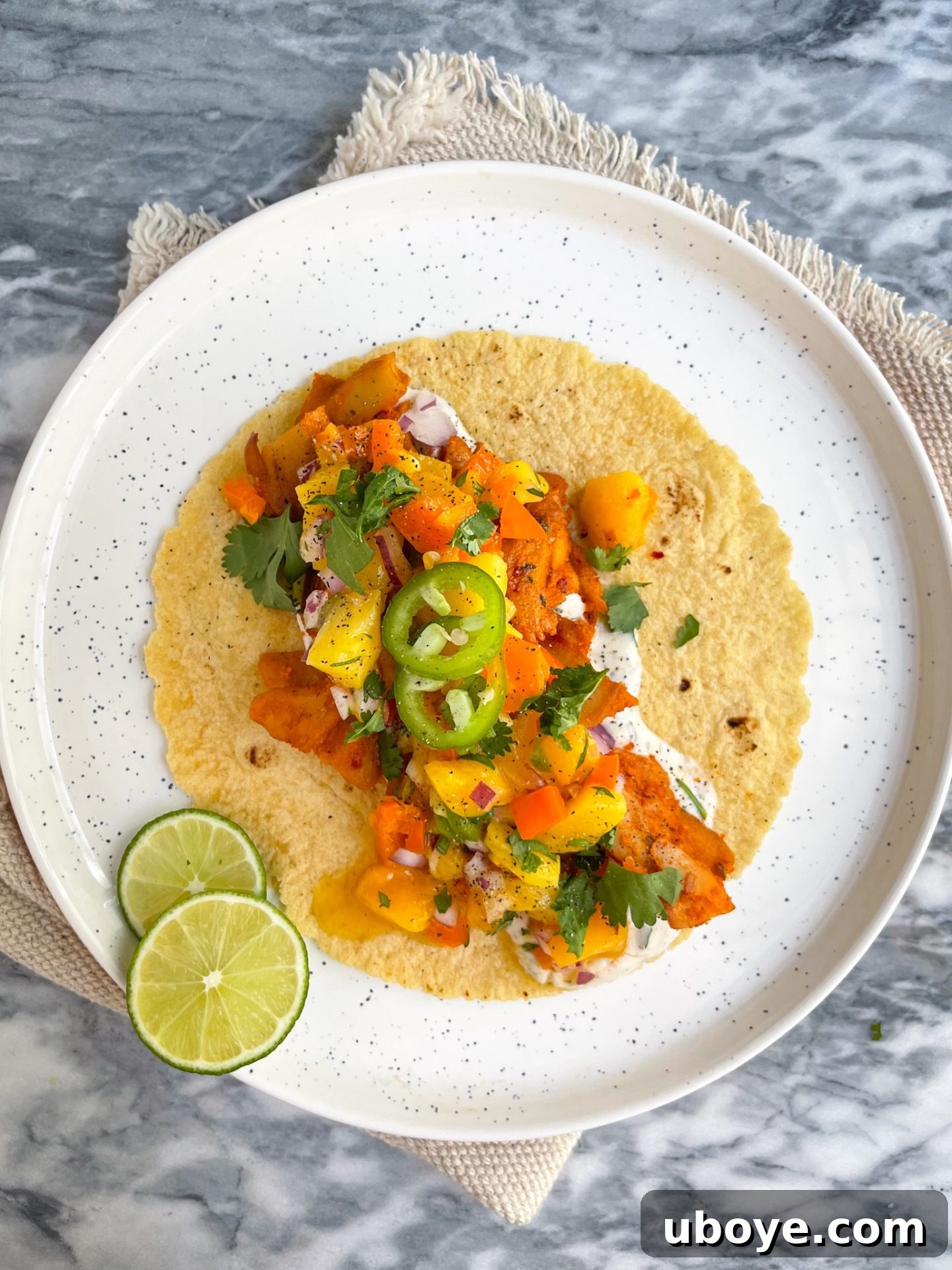 Two finished vegan chick'n tacos with mango salsa and cilantro yogurt sauce on a cutting board