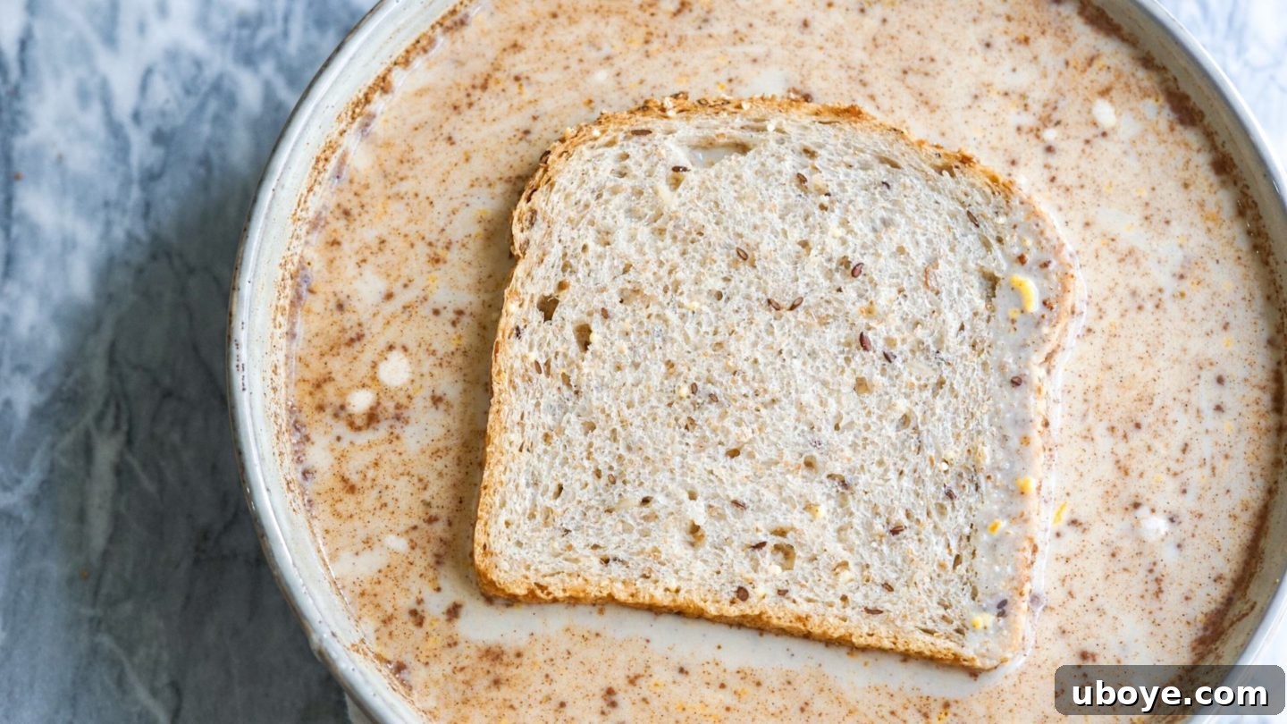 Multiple slices of day-old bread actively soaking in a vibrant yellow, rich dairy-free French toast batter within a large blue mixing bowl, ready for cooking.