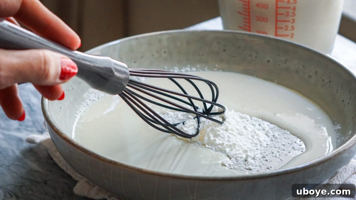 A whisk blending cornstarch, baking powder, nutritional yeast, and spices with a small amount of plant milk in a blue bowl, creating the smooth base for the vegan French toast batter.