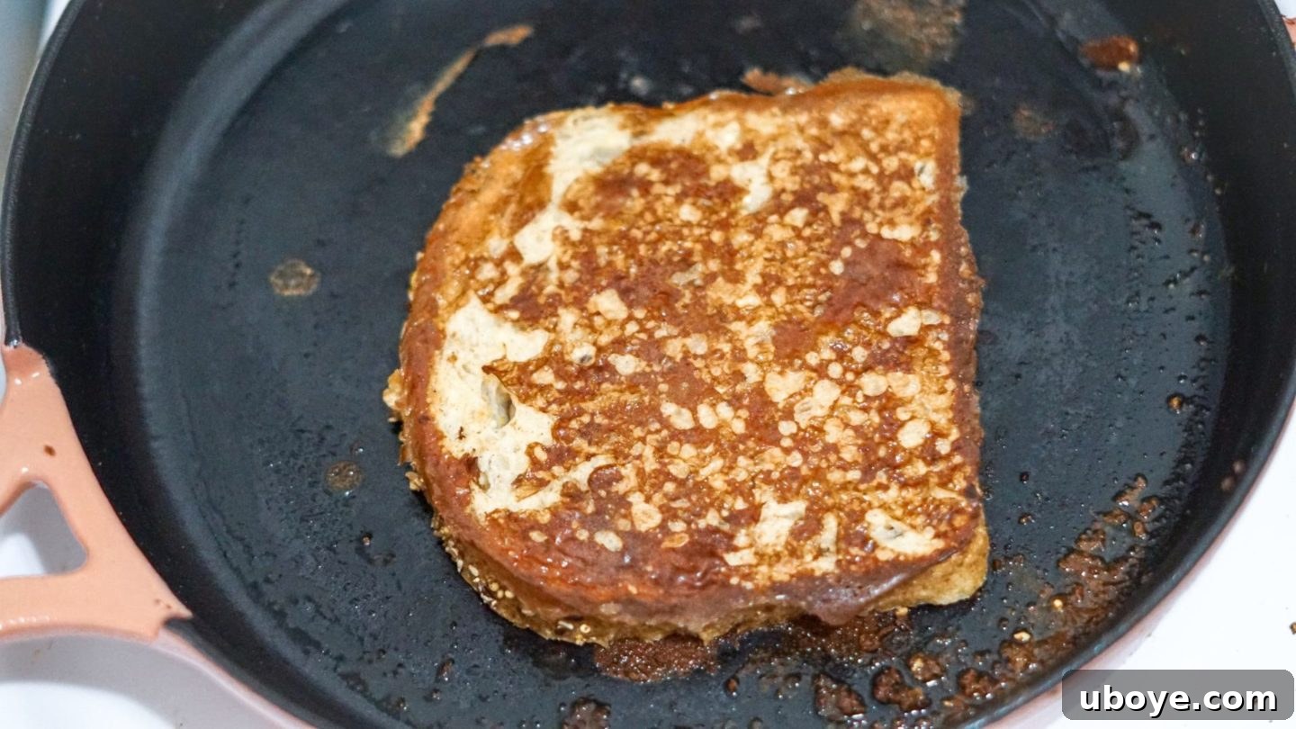 Two slices of perfectly cooking vegan French toast resting in a well-seasoned cast iron pan, showing their inviting golden-brown crust.