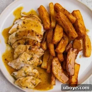 A close-up of sliced roasted chicken served with a side of crispy chips and a pool of rich gravy.