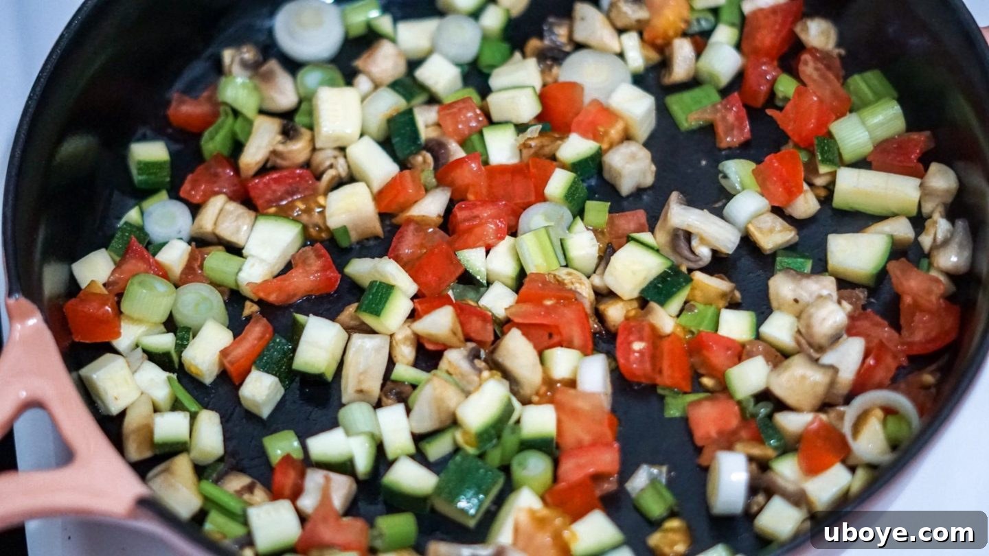 A mix of chopped vegetables, including mushrooms, onions, and zucchini, cooking in a pan to soften and release their flavors.
