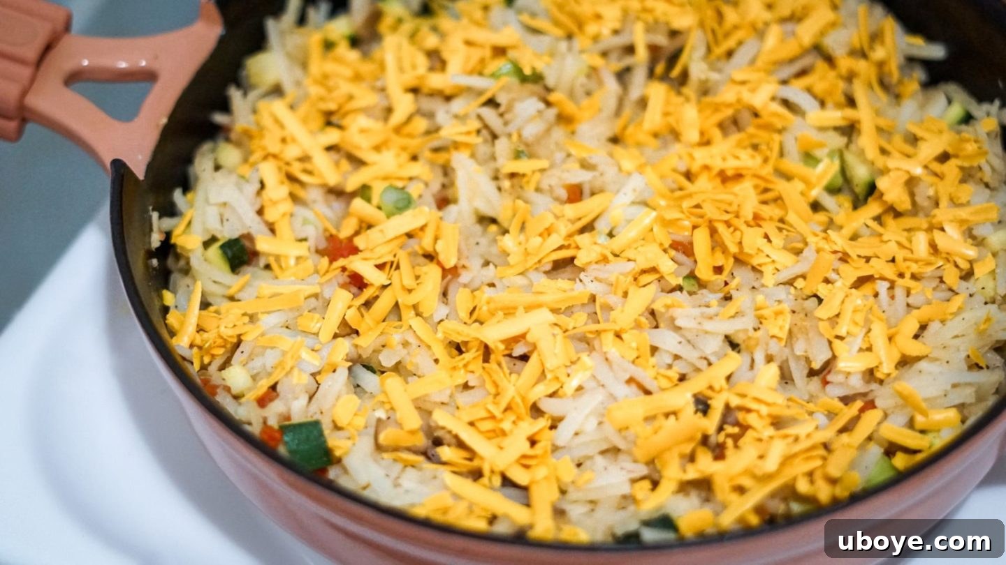 A vibrant skillet filled with vegetables, hash browns, and vegan cheese before the vegan egg is poured over and baked.