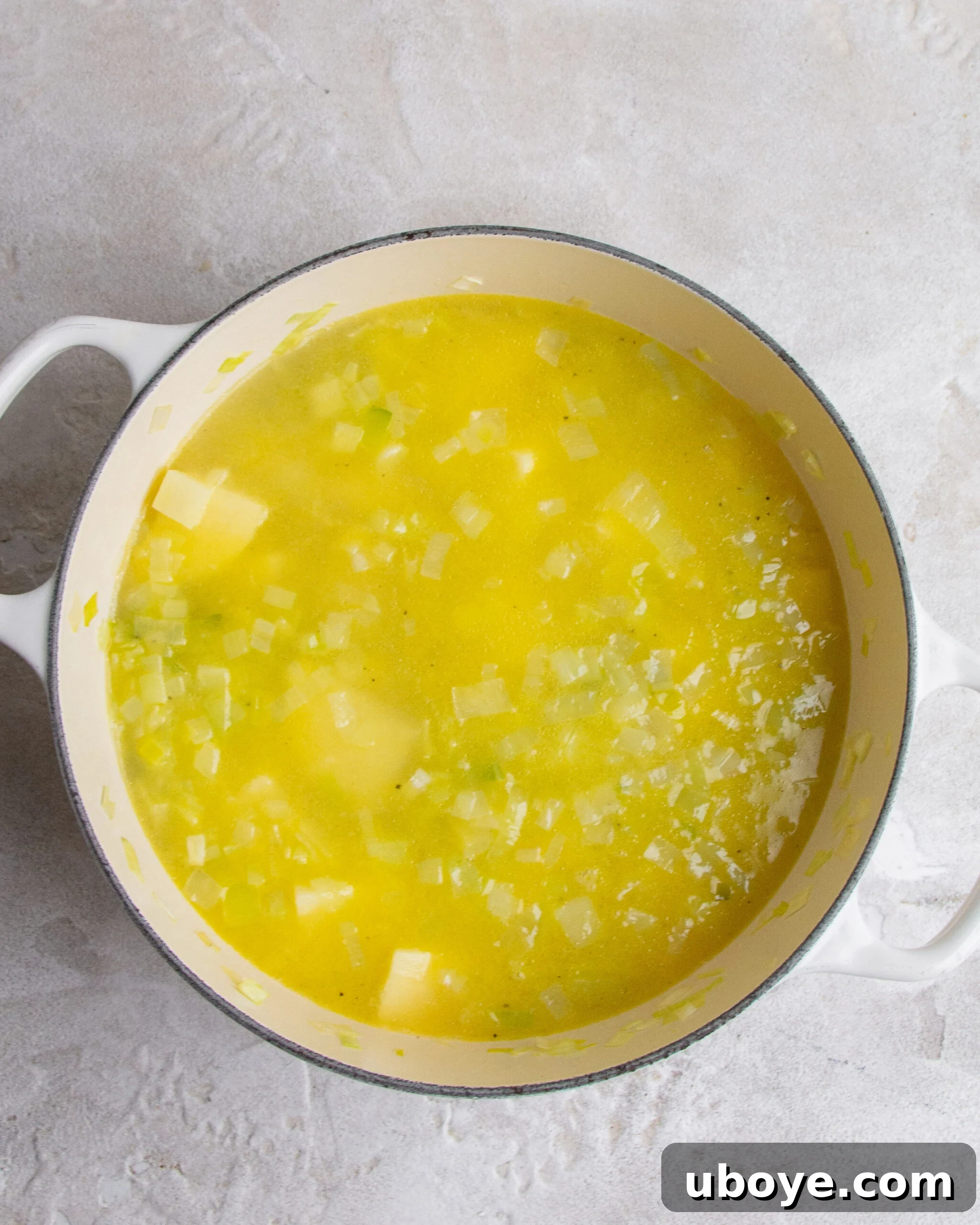 Silky Potato Leek Delight 3 A large pot filled with unblended potato and leek soup ingredients, showing chunks of potato and softened leeks simmering in a rich broth. The texture is still chunky, awaiting the blending process.