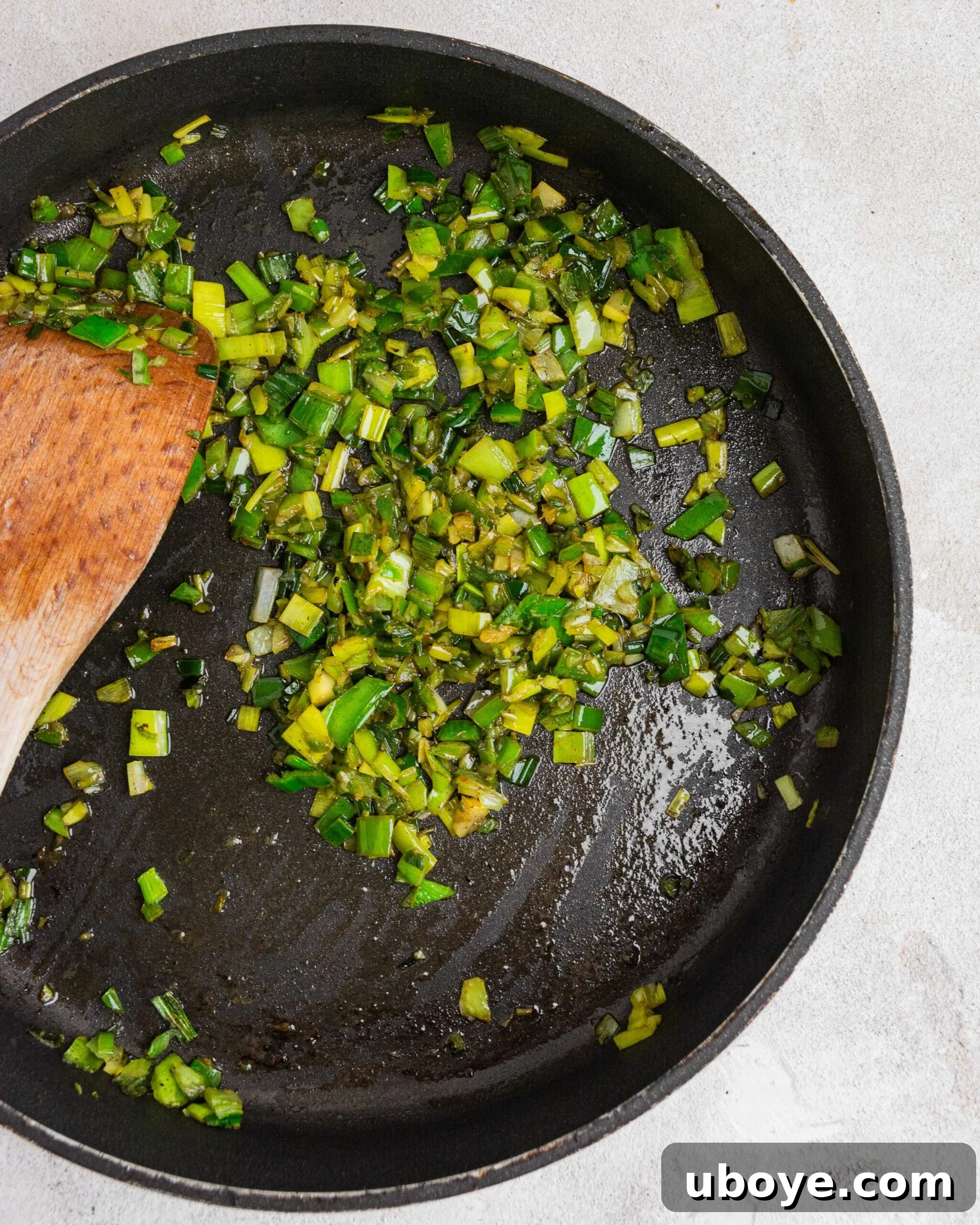 Silky Potato Leek Delight 5 Thinly sliced dark green leek tops sizzling and browning in a hot fry pan, indicating they are being crisped up for a garnish. The pan shows some residual fat, likely from bacon, enhancing their flavor.