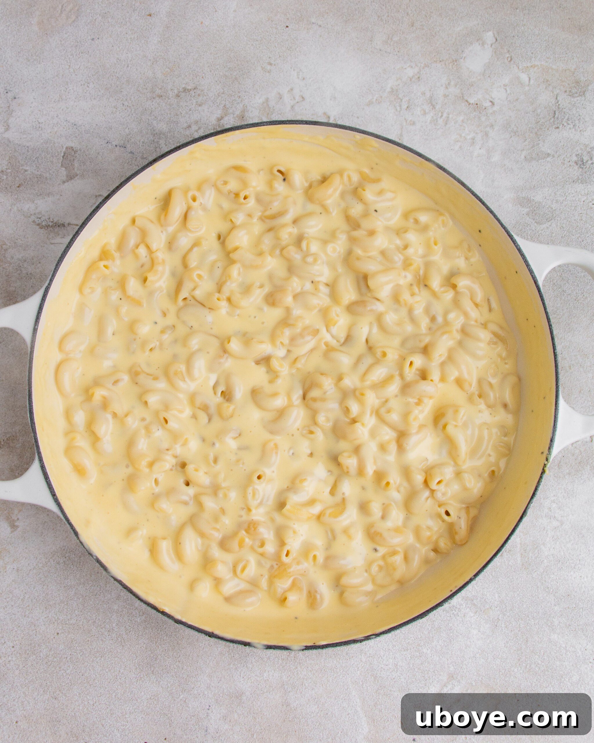 Unbaked mac and cheese with garlic confit in a large white baking tray, showing the pasta mixed with the creamy sauce.