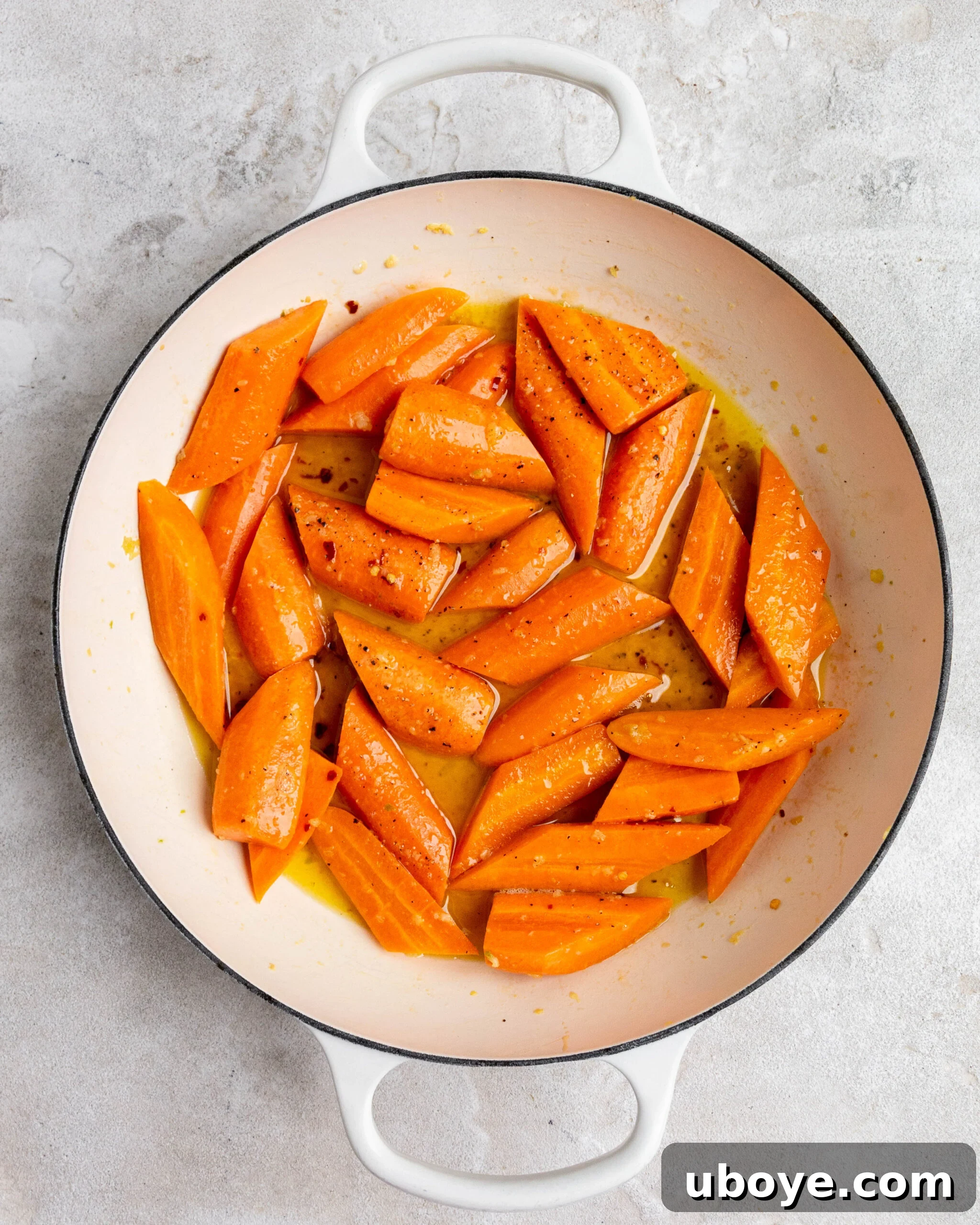 Sliced and peeled carrots sit in large white roasting pan with butter and honey. 
