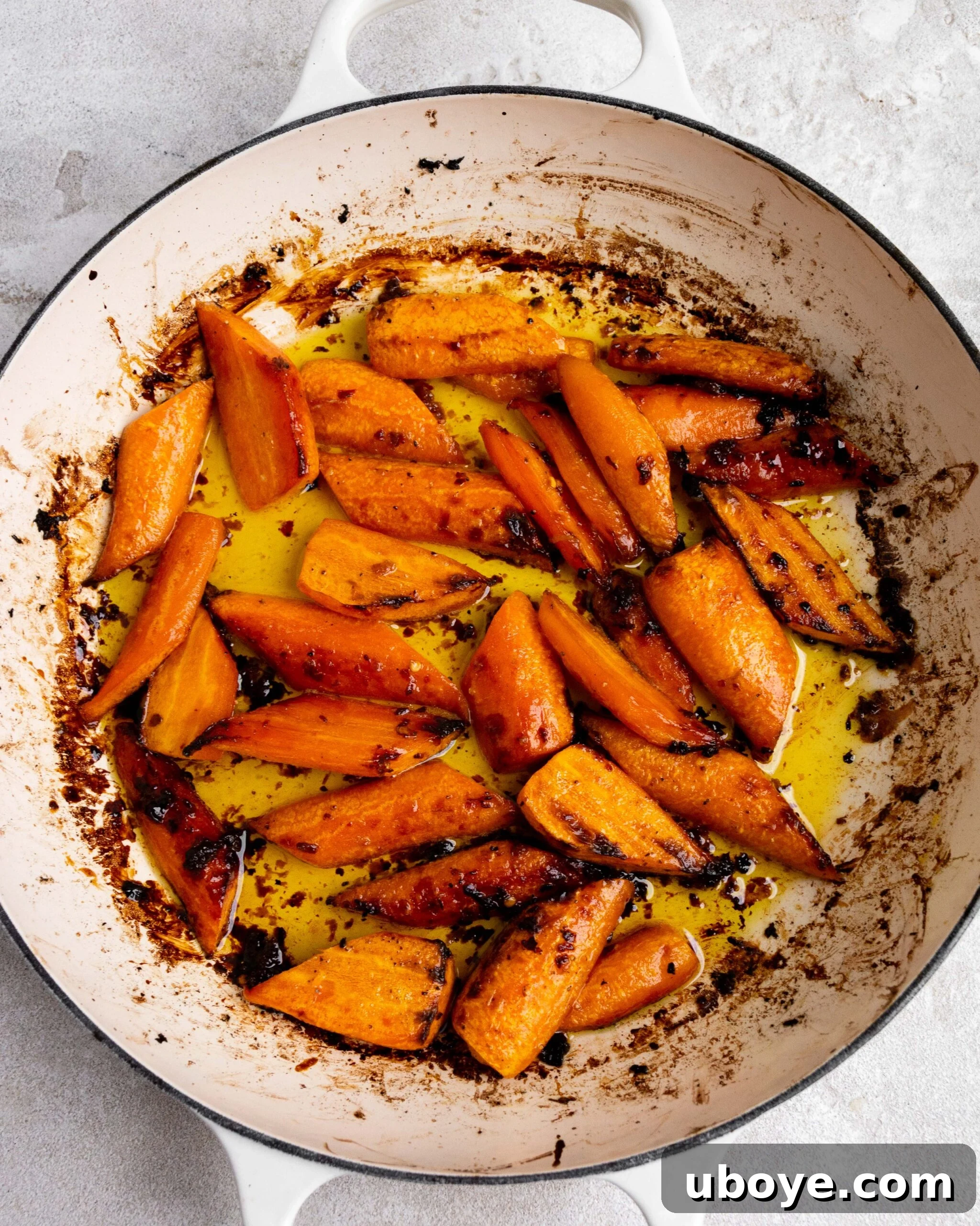 Sliced and peeled carrots sit in large white roasting pan with butter and honey. They have been roasted. 
