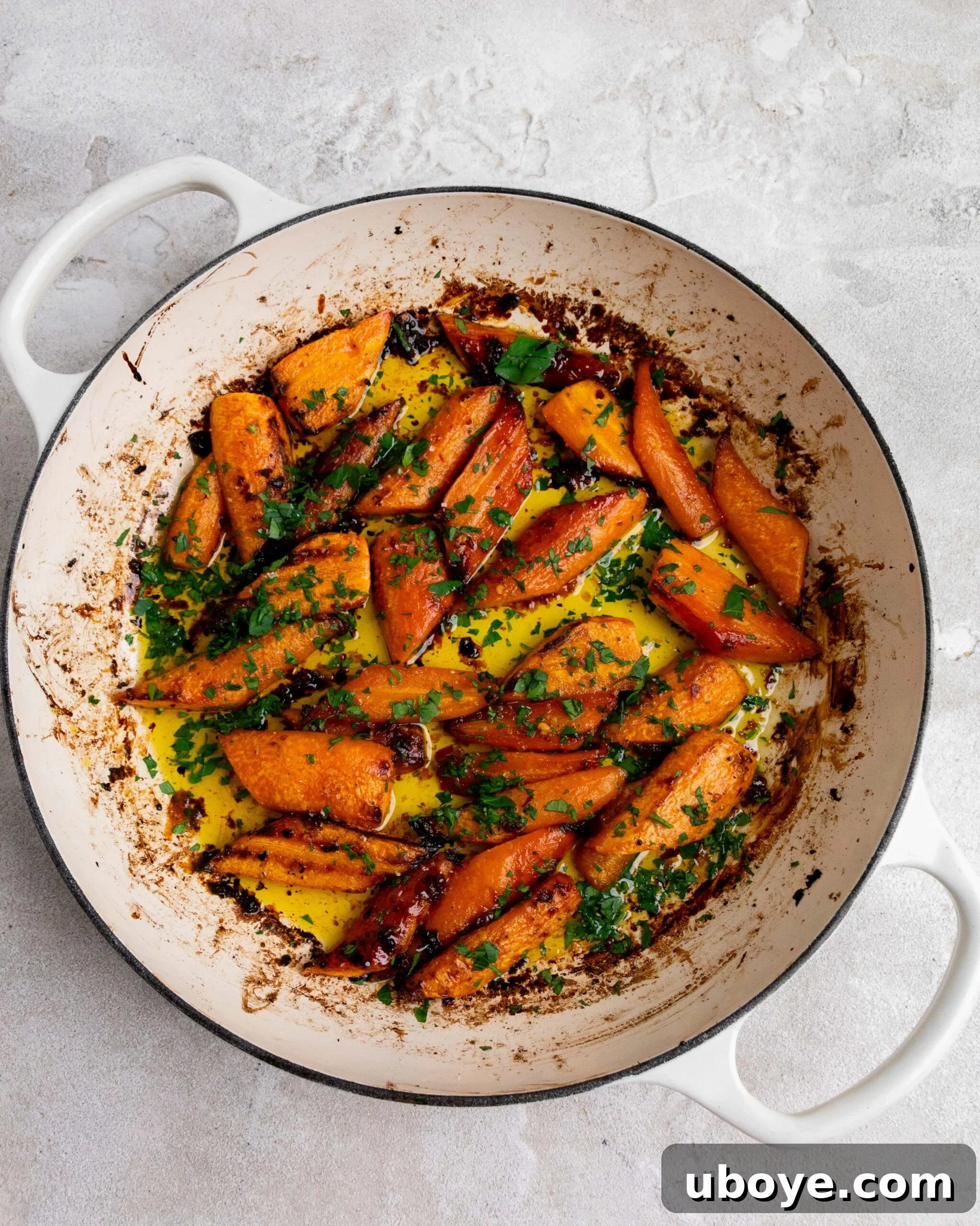 Sliced and peeled carrots sit in large white roasting pan with butter and honey. They have been roasted and been garnished with fresh parsley.