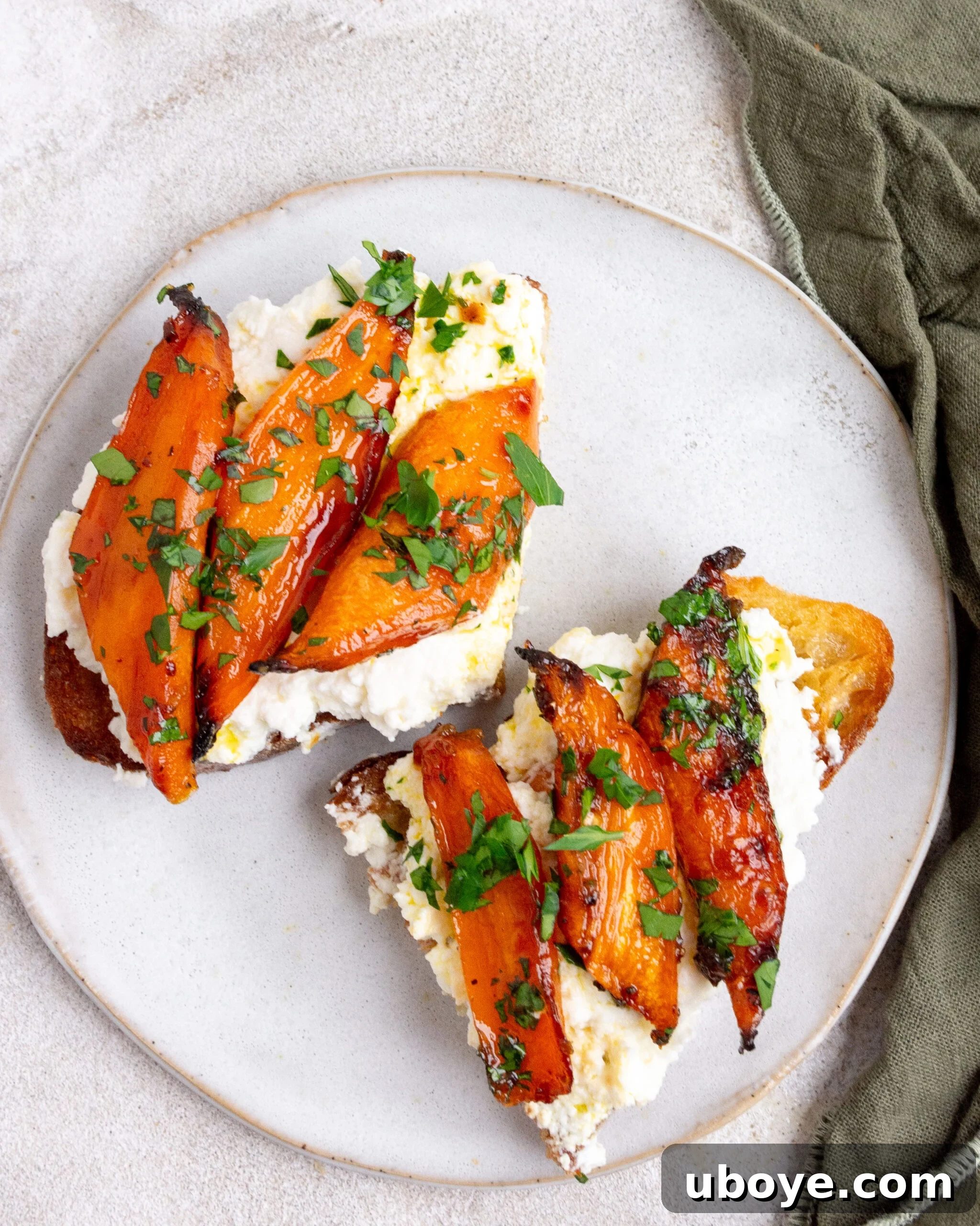 Hot honey roasted carrots sit on toast with ricotta. They are on a small white plate. 
