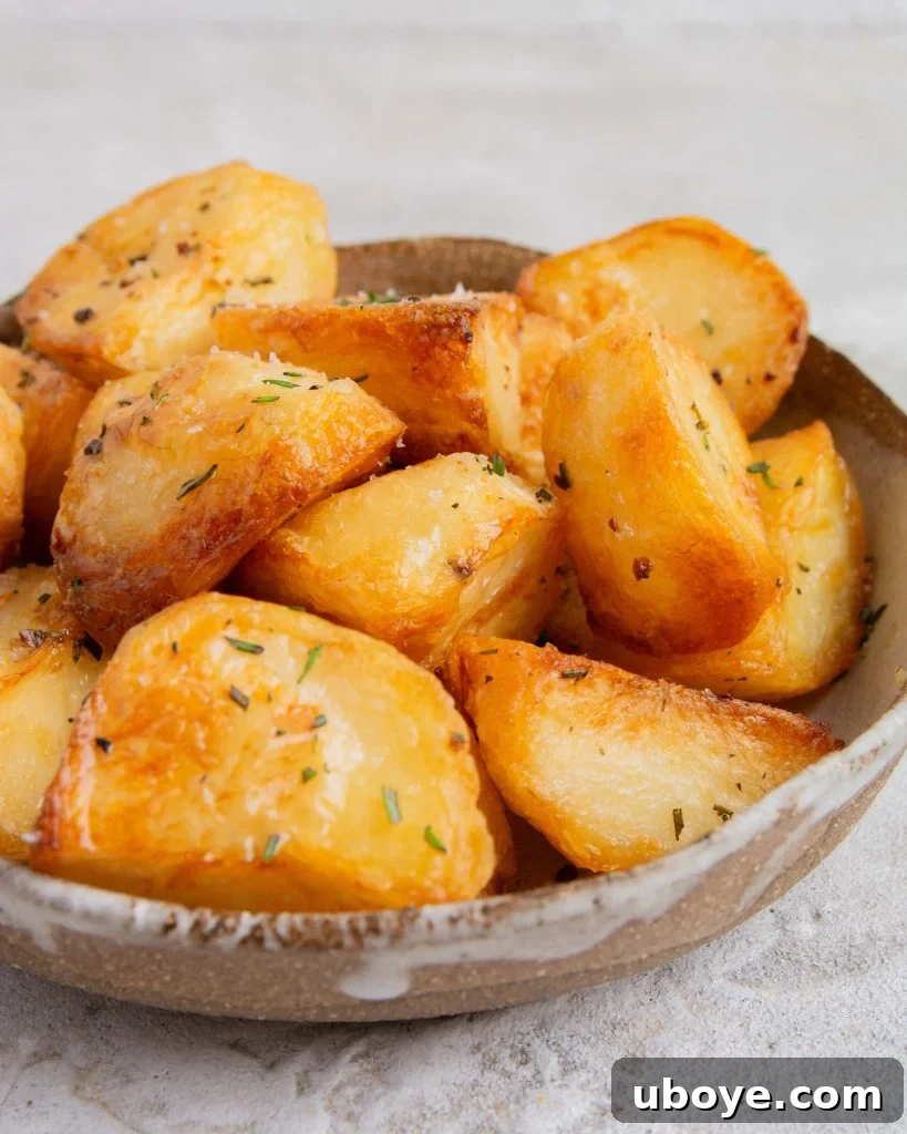 A bowl of exquisitely crispy duck fat roasted potatoes, garnished with fresh rosemary, ready to be served as a festive side dish.