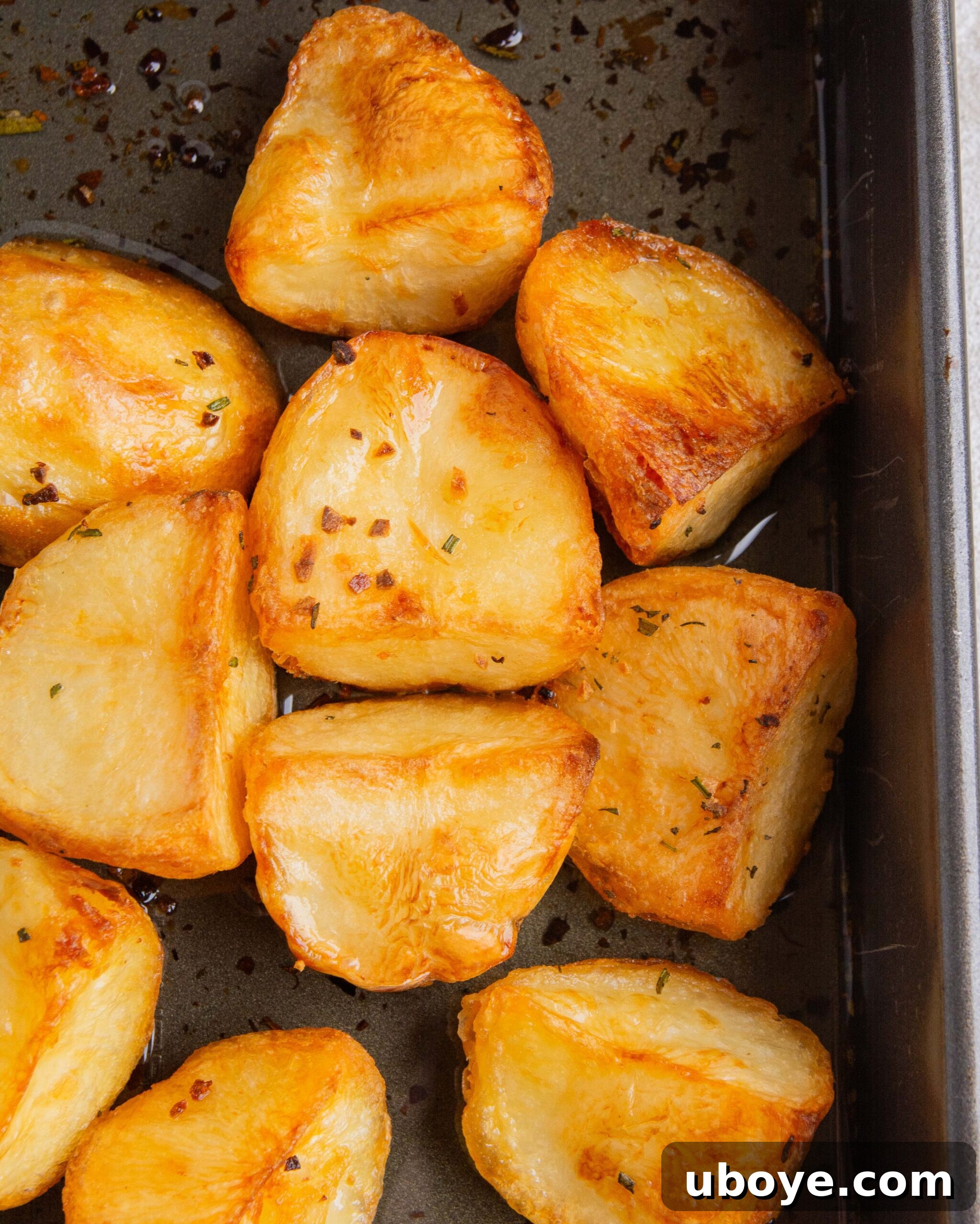 A baking tin filled with perfectly crispy duck fat roasted potatoes, glistening golden-brown and ready for the final aromatic additions.
