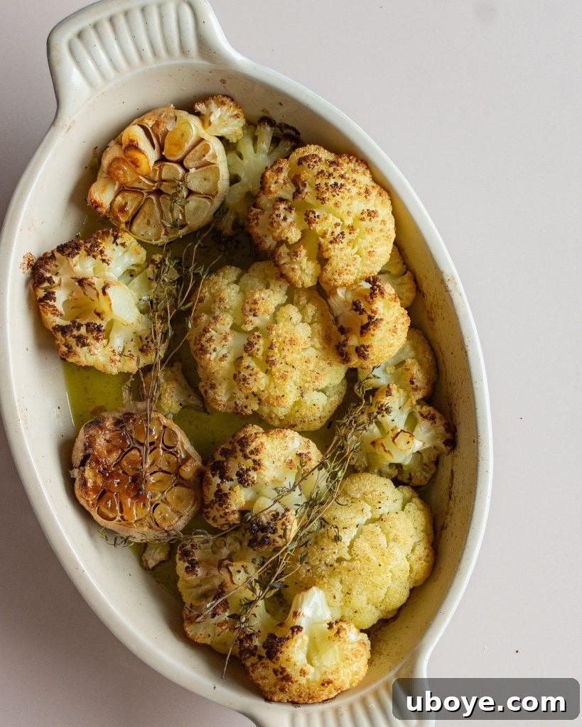 Creamy Cauliflower Delight 3 Close-up of golden roasted cauliflower florets and garlic bulbs on a baking sheet.