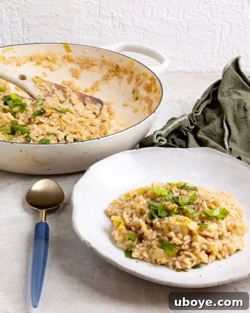 Creamy Leek Risotto 2 A bowl of creamy leek risotto, garnished with crispy fried leek tops, sits elegantly in front of a larger pot of risotto. A blue spoon rests nearby.