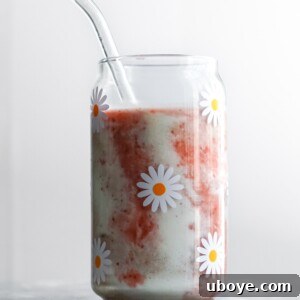Strawberry smoothie in a glass with a straw, garnished with coconut cream