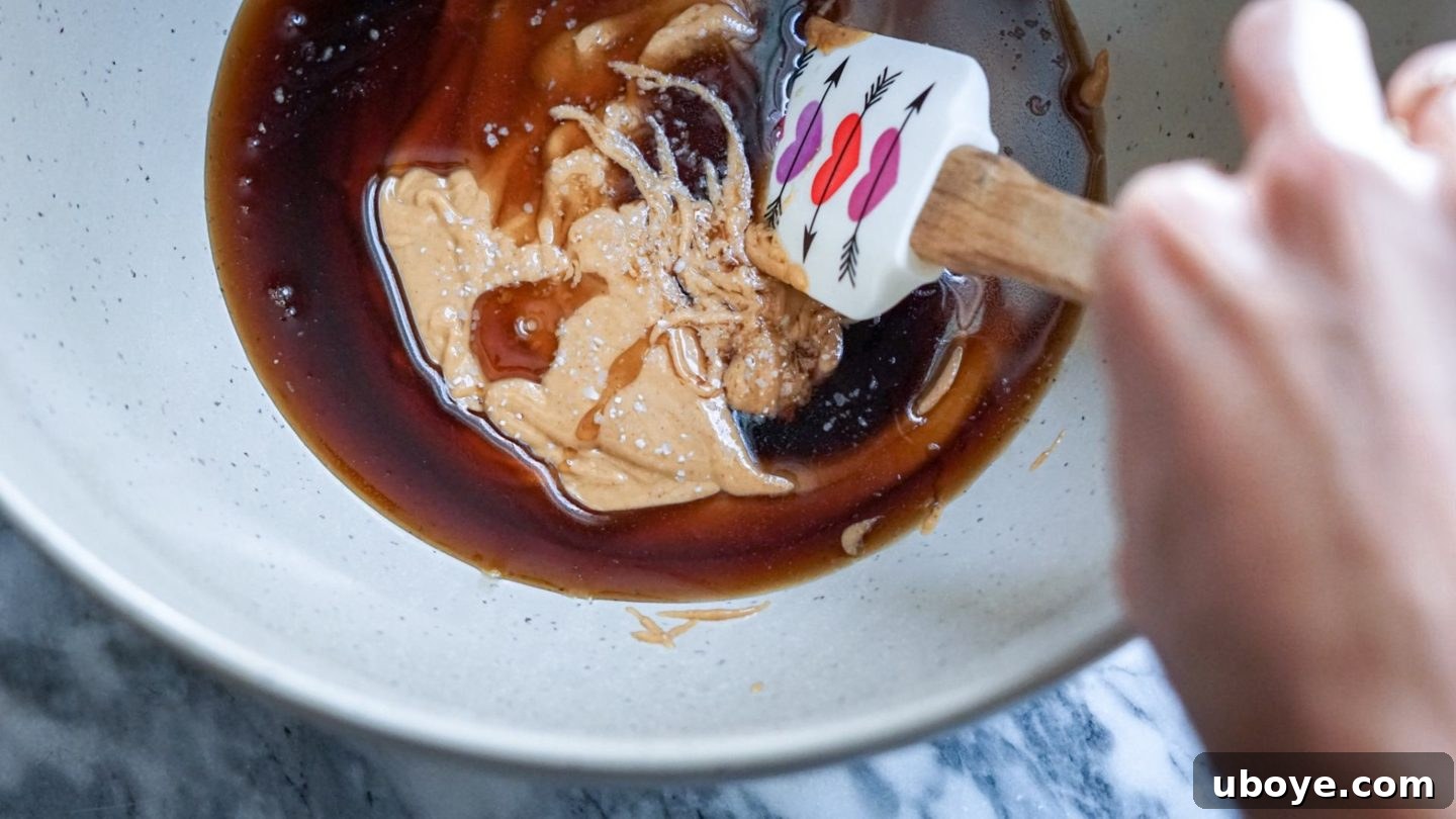 Bee-Free Honey Nut Cereal Bars 5 Peanut butter, maple syrup, and other liquid ingredients being mixed in a large bowl.