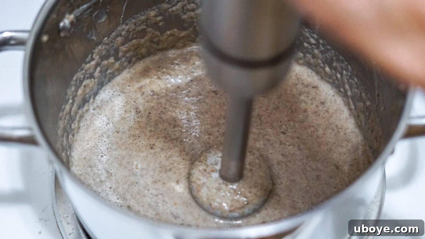 Creamy Mushroom Dream Pasta 5 An immersion blender actively blending the creamy mushroom sauce in a pot, transforming the ingredients into a smooth, velvety texture.
