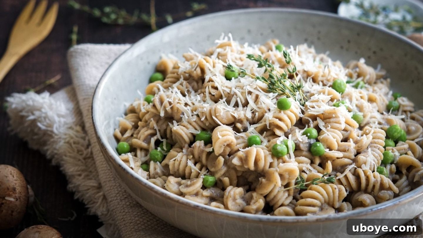 Creamy Mushroom Dream Pasta 6 Cooked rotini pasta, vibrant green peas, and vegan parmesan cheese are tossed into the creamy mushroom sauce in a large pot, ready to be combined for a delicious meal.