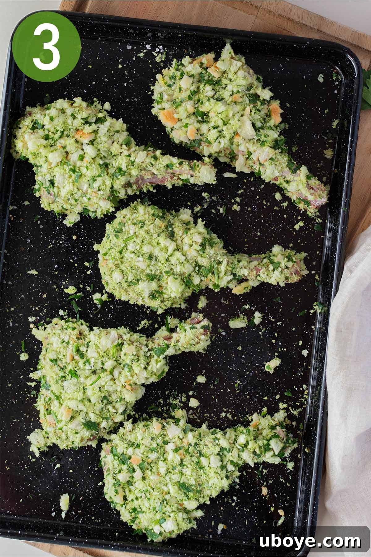 A hand pressing herbed breadcrumbs onto a lamb cutlet, ensuring an even and thorough coating.