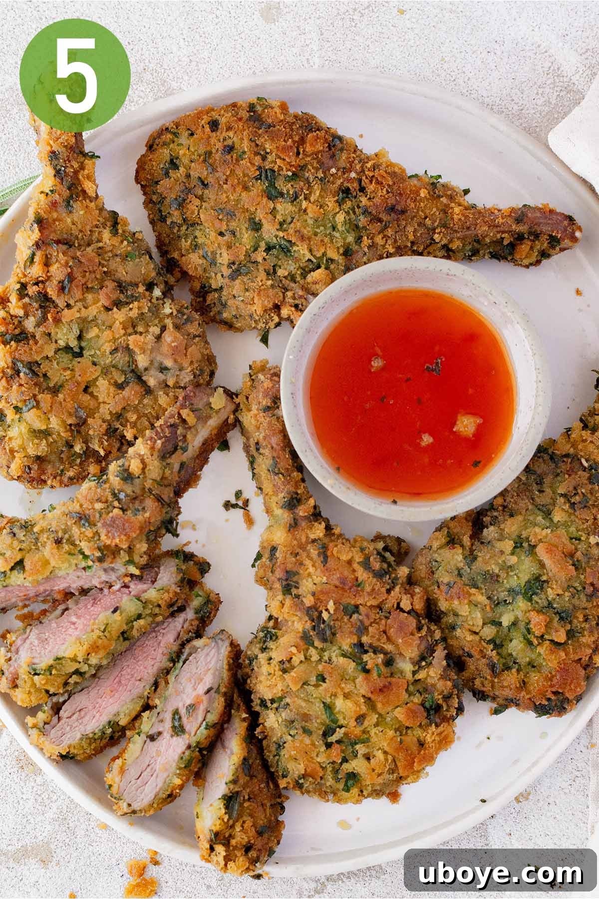 A serving of whole and sliced crumbed lamb cutlets, revealing the juicy interior, with a side of dipping sauce.