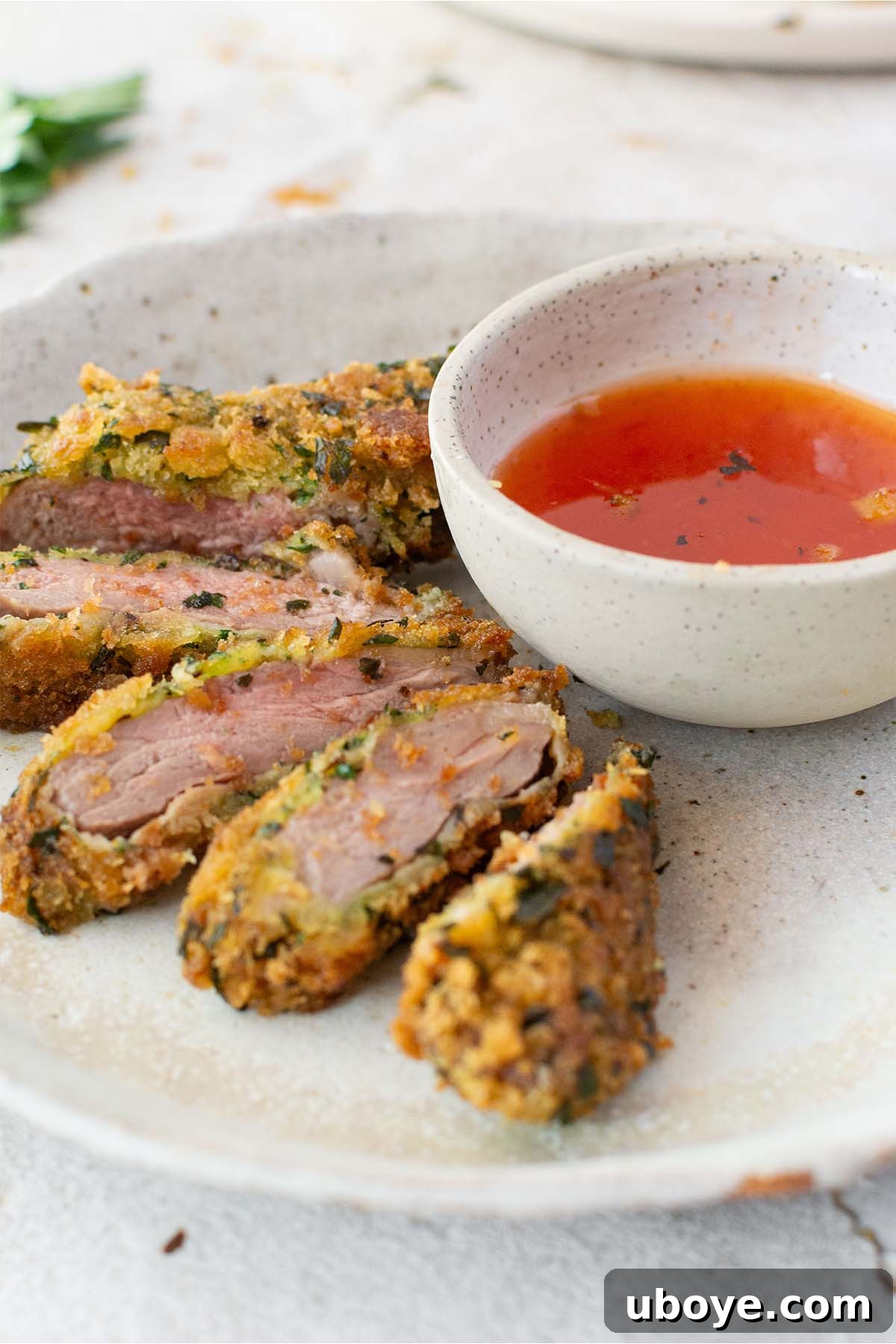 A vibrant platter featuring perfectly sliced crumbed lamb cutlets, revealing their juicy interior, accompanied by a small bowl of creamy dipping sauce.