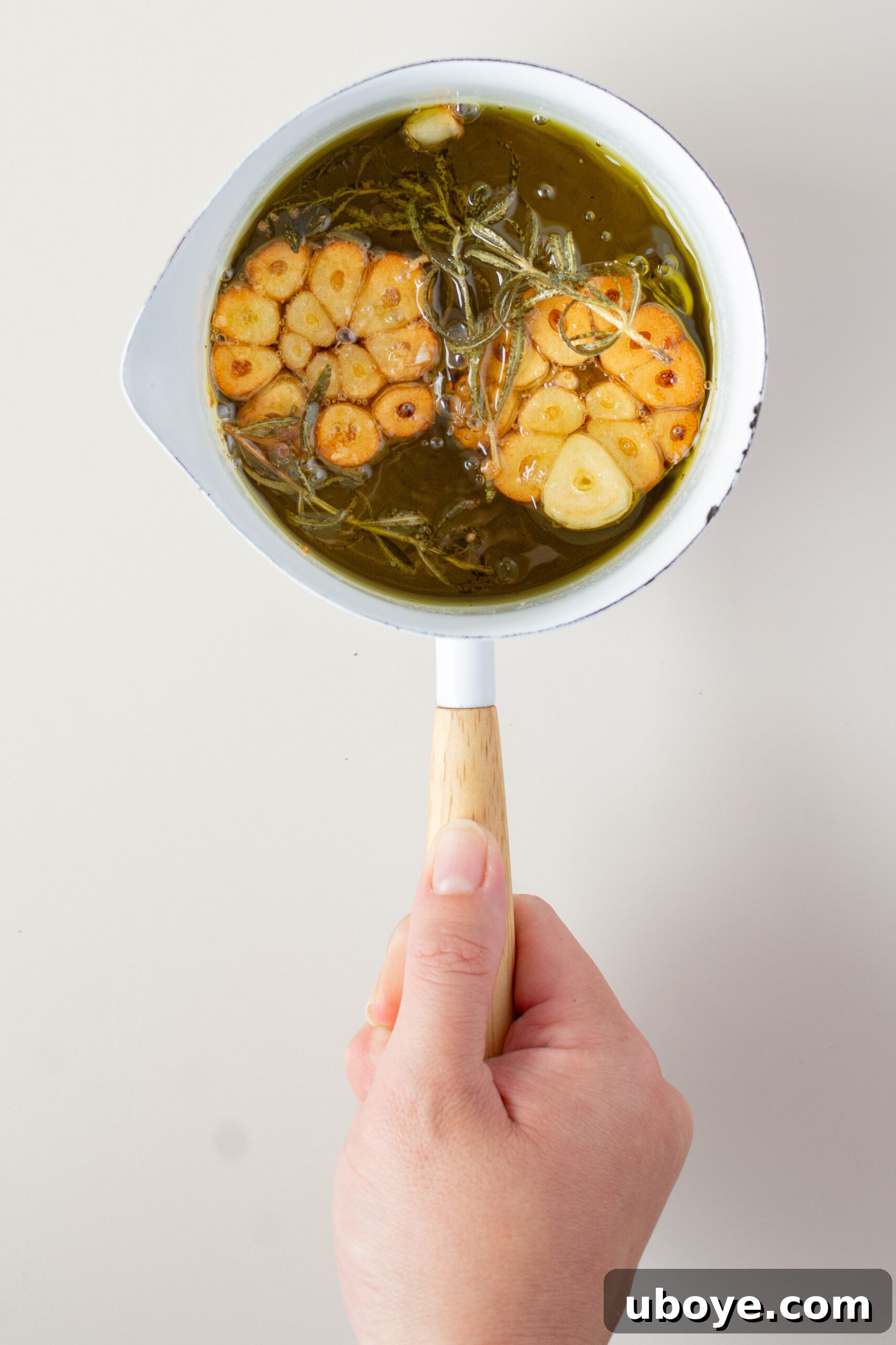 Small white pot with golden, infused olive oil, cooked garlic, and rosemary.