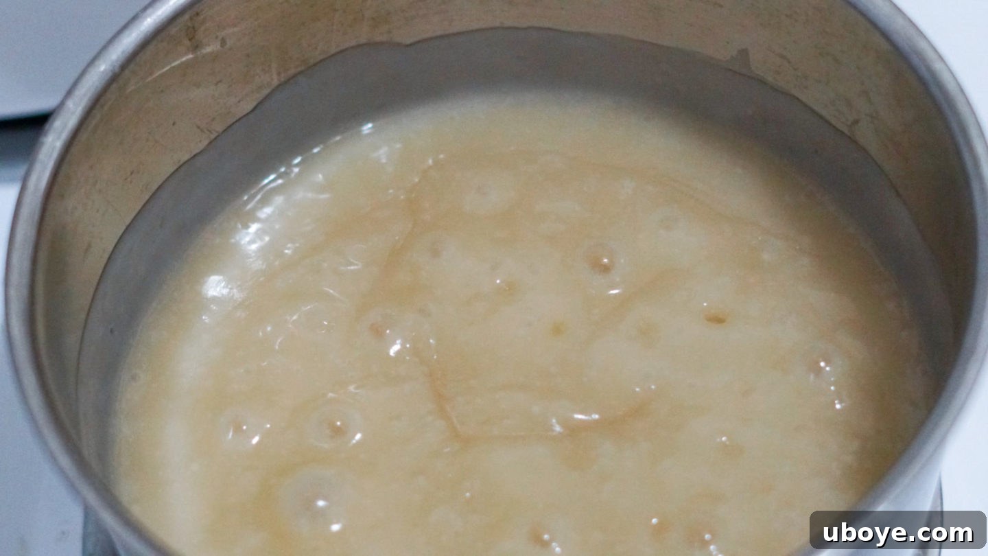 A saucepan on a stove with a creamy mixture being whisked, showing the pudding thickening.