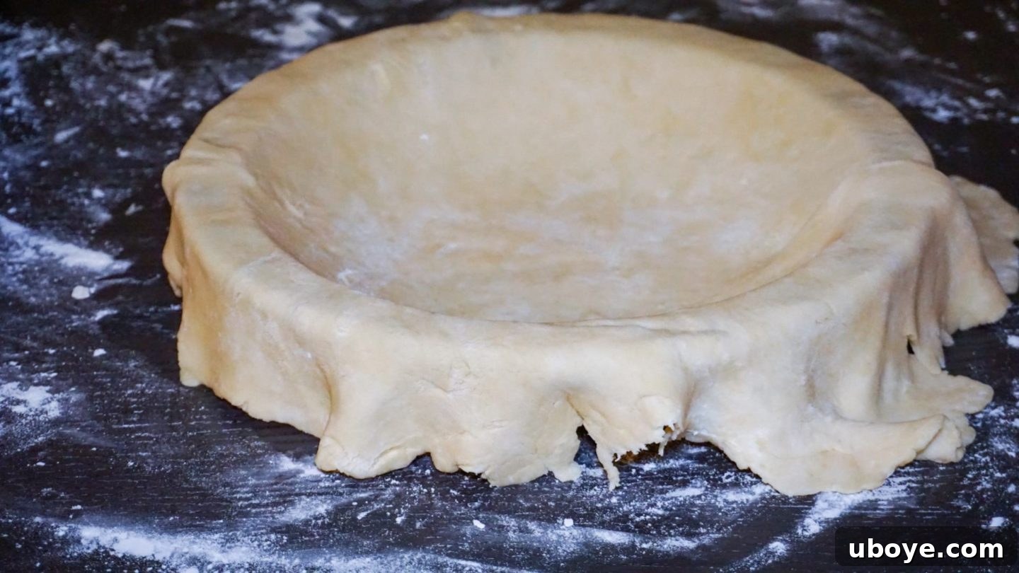 Grandma's Blueberry Comfort 8 Pie dough gently placed into a pie dish, with excess dough hanging over the edges, ready for shaping.