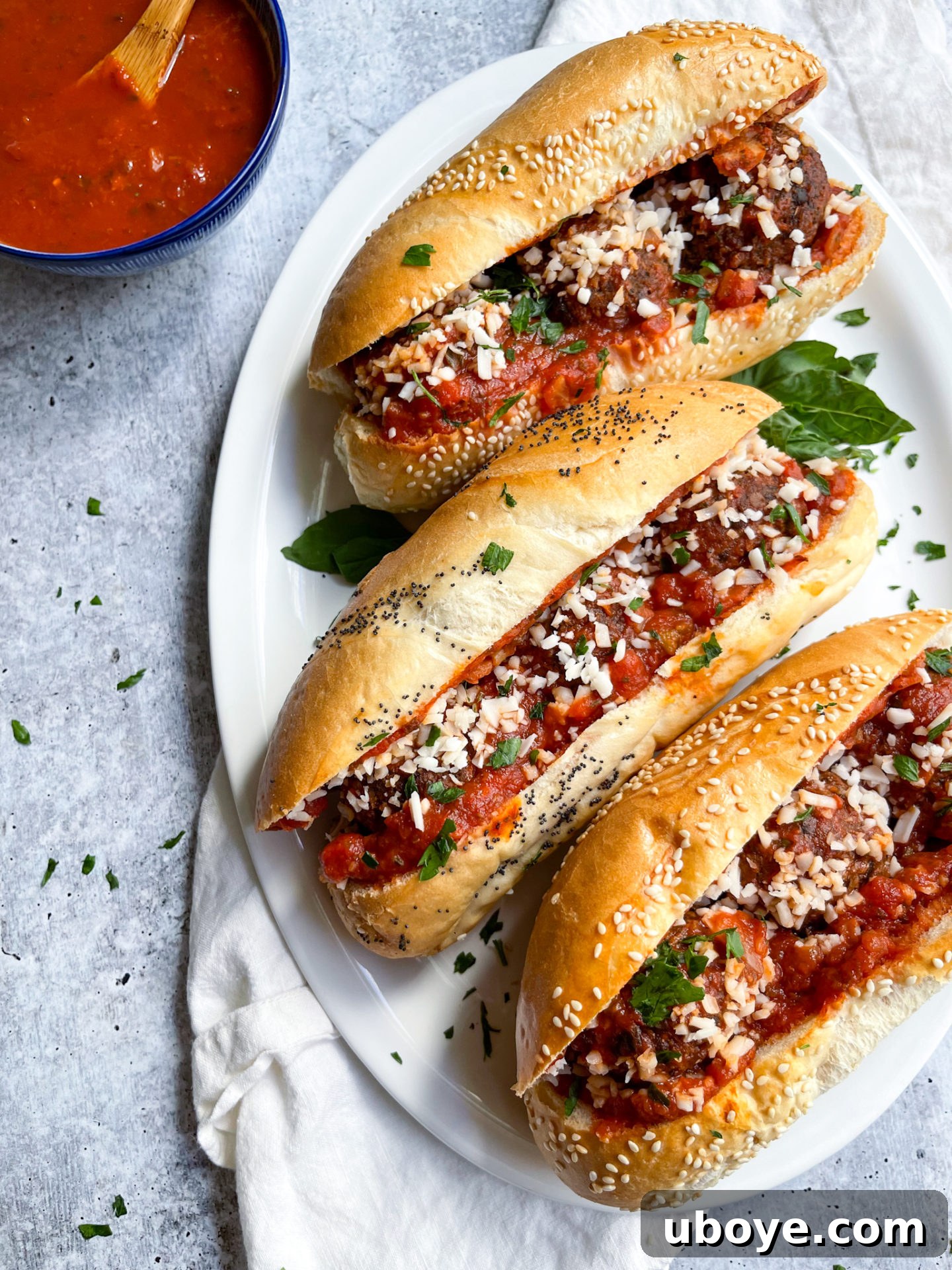 Game-Changing Lentil Meatball Heroes 2 Three meatball sub sandwiches on a white plate, garnished with fresh basil.