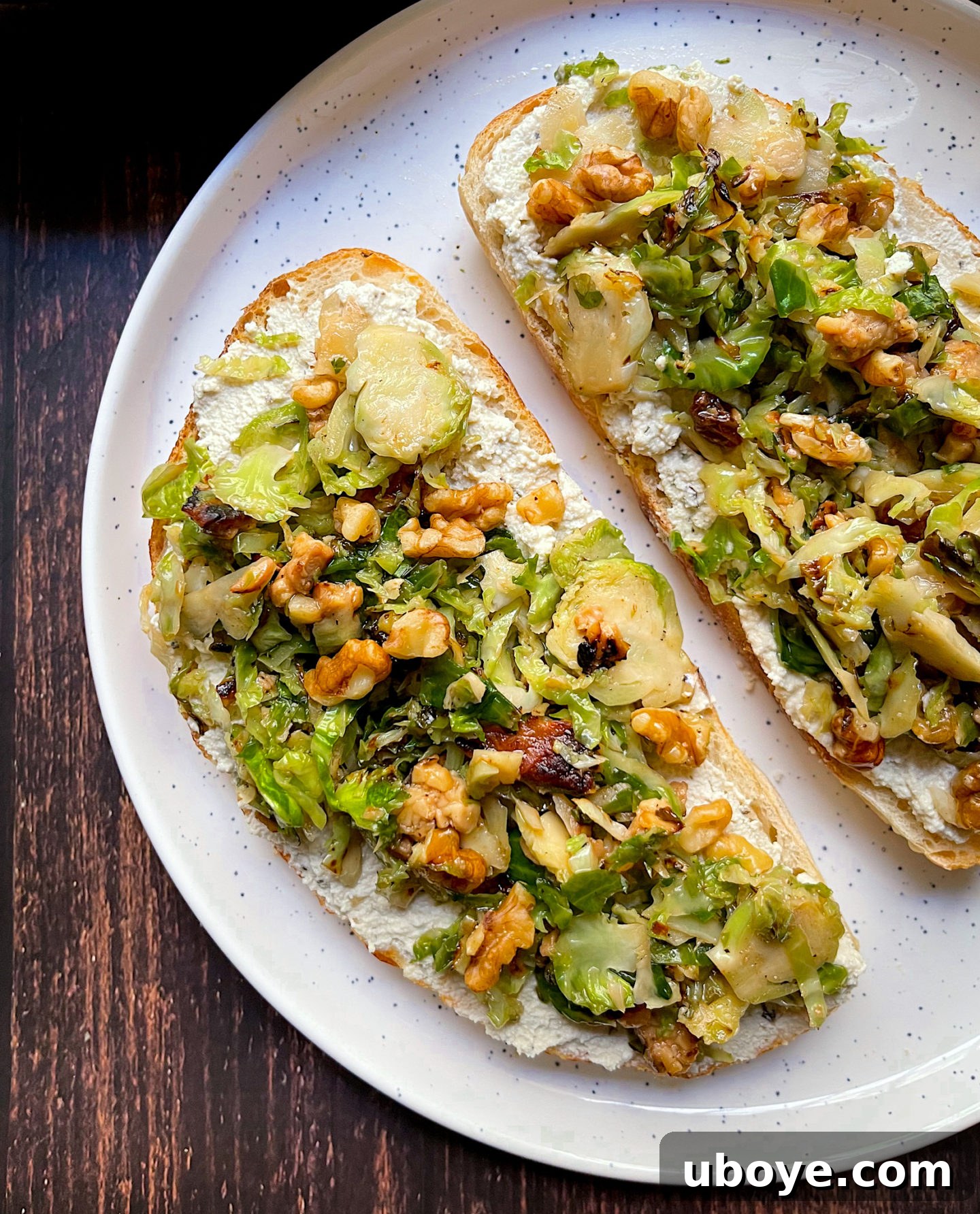 Close-up shot of sautéed brussel sprouts and tempeh bacon heaped on a slice of sourdough bread spread with creamy vegan ricotta.
