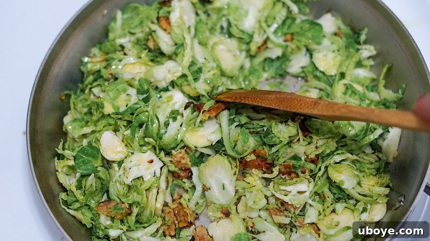 Close-up of shredded brussel sprouts and crumbled tempeh bacon being sautéed in a hot pan with olive oil.