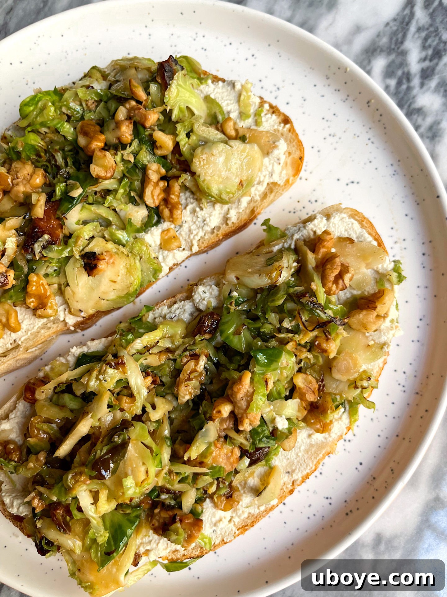 A beautifully presented plate of brussel sprouts with raisins and walnuts on creamy vegan ricotta toast, ready to be enjoyed.