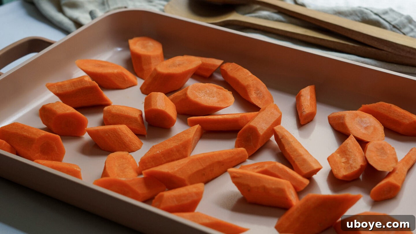 Carrot pieces seasoned with salt and pepper, drizzled with olive oil on a baking sheet, ready for roasting.