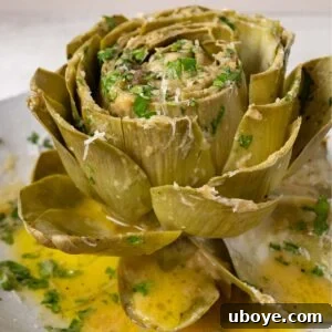 A close-up of a steamed artichoke half, generously topped with melted garlic butter, grated Parmesan cheese, and fresh herbs.