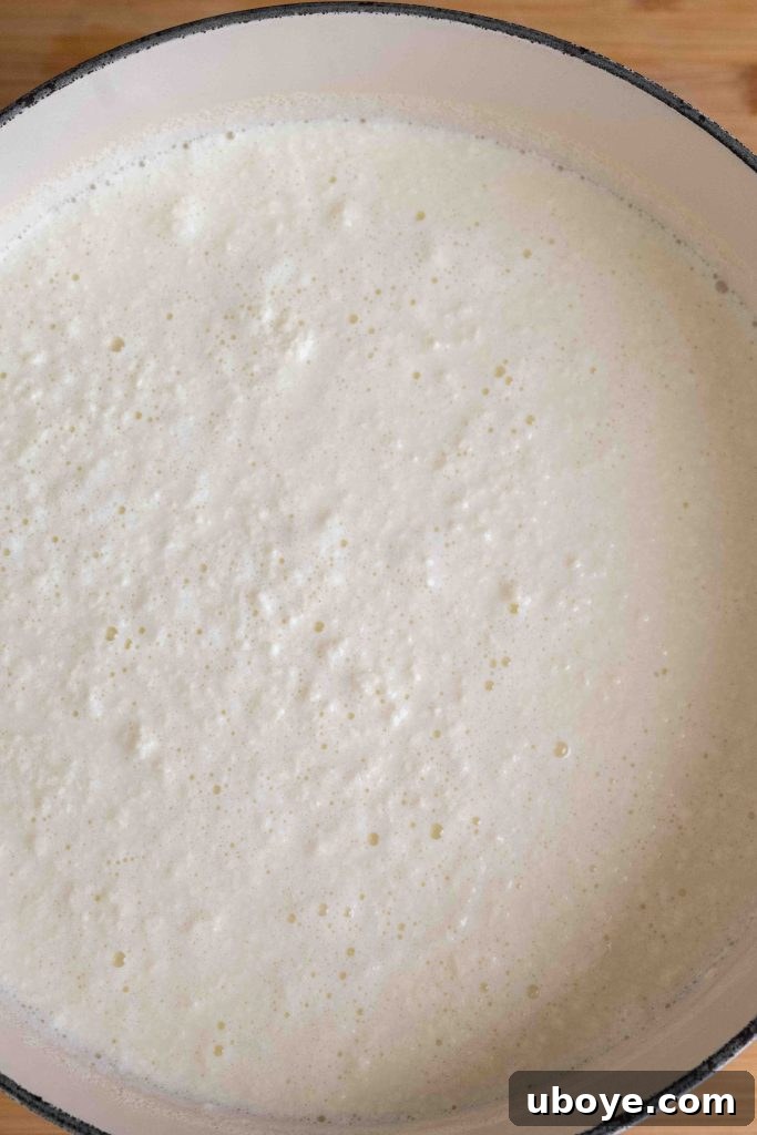 A generous scoop of freshly made homemade ricotta cheese resting on a straining cloth, with the whey visibly dripping into a bowl below.
