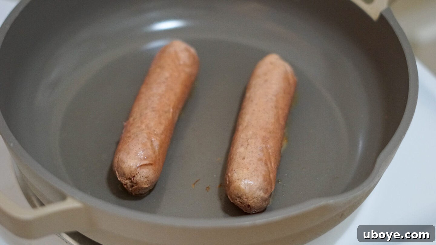 Vegan sausages browning in a large frying pan before being sliced and added to pasta.