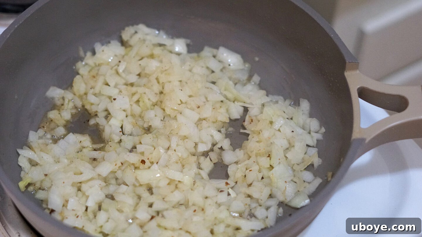 Sautéed translucent onions in a frying pan with minced garlic, forming the aromatic base for the Cajun pasta sauce.