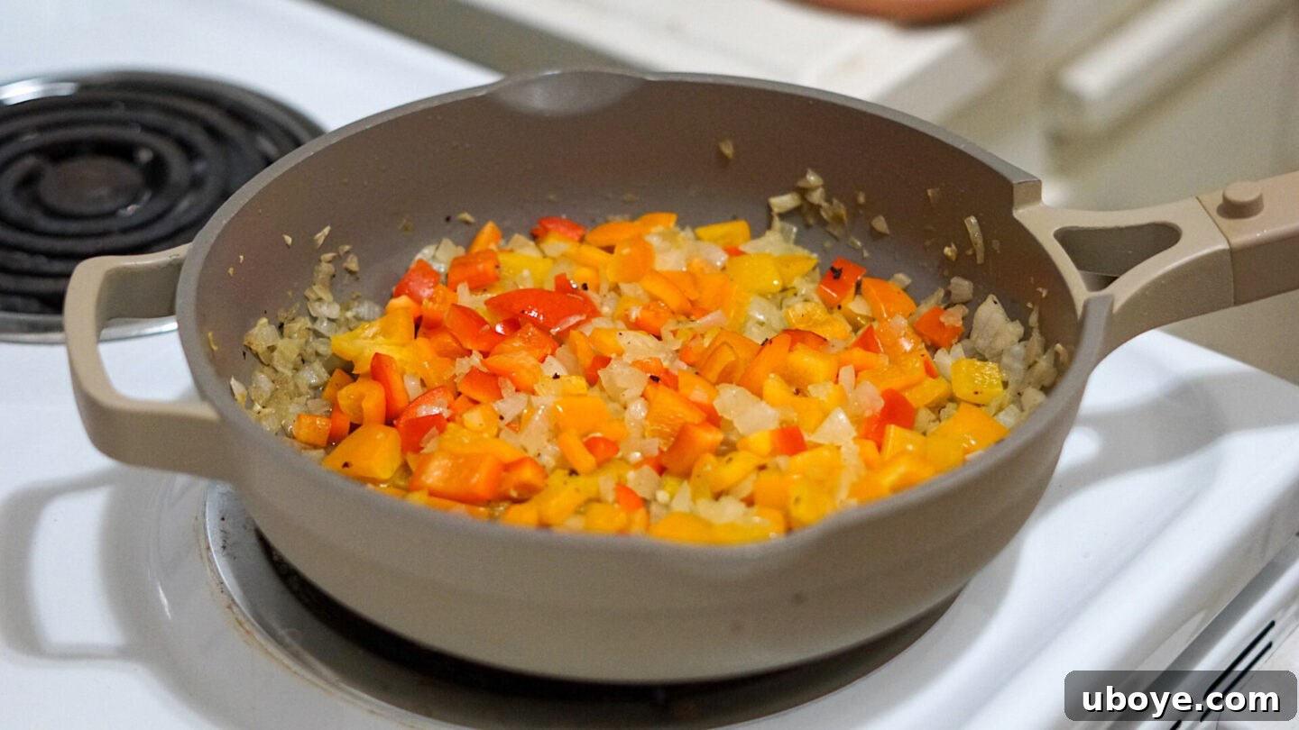 Chopped red bell peppers added to sautéed onions and garlic in a pan, ready for the next step of the Cajun pasta.